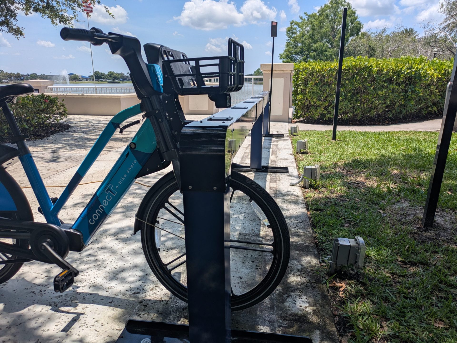 Blue e-bike docked at an outdoor Juise charging station beside a park path