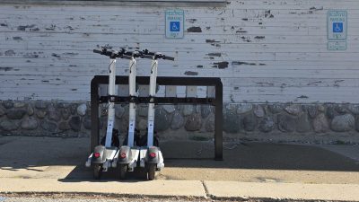 Three e-scooters docked in a Juise charging rack on a city sidewalk