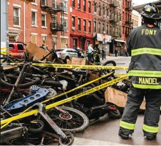 FDNY firefighter beside burned e-bikes behind caution tape after a lithium-ion battery fire